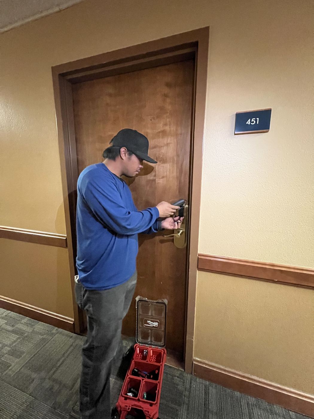 Technician programming a SALTO smart lock on a numbered unit door in a lodge corridor